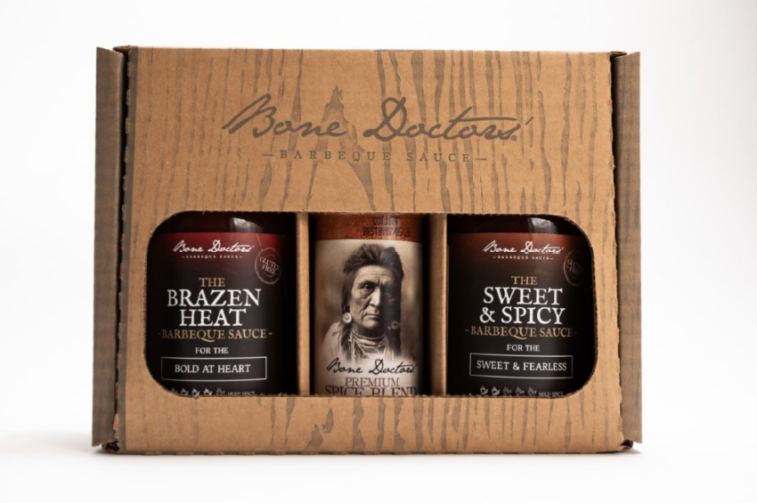 A gift set, wood-styled box with two bottles of Bone Doctors' Barbecue Sauce and a bottle of spice blend on a white background.