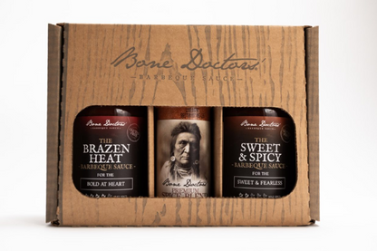 A gift set, wood-styled box with two bottles of Bone Doctors' Barbecue Sauce and a bottle of spice blend on a white background.