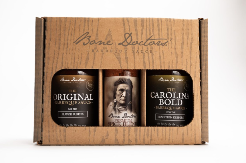 A gift set, wood-styled box with two bottles of Bone Doctors' Barbecue Sauce and a bottle of spice blend on a white background.